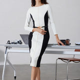 A professional woman wearing a sophisticated black and white color-block midi dress, featuring slimming side panels, long sleeves, and an elegant black belt with a gold buckle for a modern executive office look.