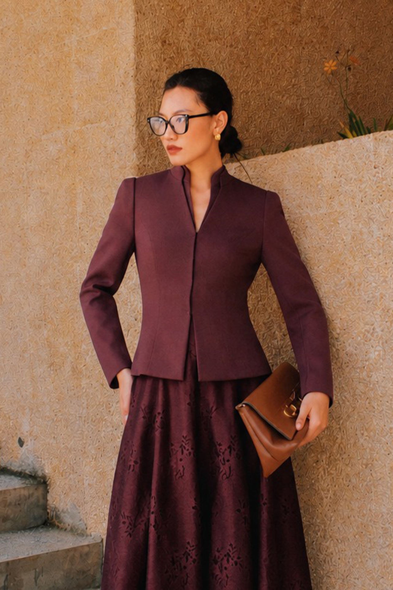 A professional Asian woman wearing glasses and an elegant deep burgundy tailored blazer featuring a sophisticated stand collar with a split V-neckline, structured shoulders, and a clean minimalist front.