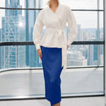 A stylish woman posing against a city skyline wearing a navy blue wrap blouse with golden ginkgo leaf print tied at the waist, paired with tailored mustard yellow wide-leg trousers.