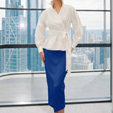 A stylish woman posing against a city skyline wearing a navy blue wrap blouse with golden ginkgo leaf print tied at the waist, paired with tailored mustard yellow wide-leg trousers.