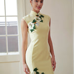 A professional woman wearing a stunning pale yellow sleeveless dress, featuring a traditional mandarin collar, exquisite white floral embroidery appliques along the neckline and hem, and an elegant side slit for a sophisticated modern oriental look.
