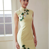 A professional woman wearing a stunning pale yellow sleeveless dress, featuring a traditional mandarin collar, exquisite white floral embroidery appliques along the neckline and hem, and an elegant side slit for a sophisticated modern oriental look.