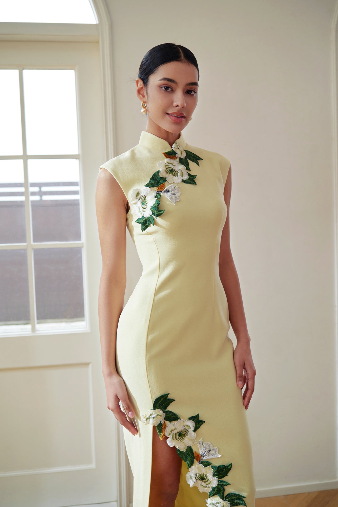 A professional woman wearing a stunning pale yellow sleeveless dress, featuring a traditional mandarin collar, exquisite white floral embroidery appliques along the neckline and hem, and an elegant side slit for a sophisticated modern oriental look.