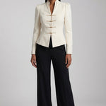 A sophisticated woman enjoying coffee in Paris wearing an elegant cream white modern qipao suit, featuring a mandarin collar blazer with traditional frog buttons and a matching pleated skirt for a quiet luxury oriental look.