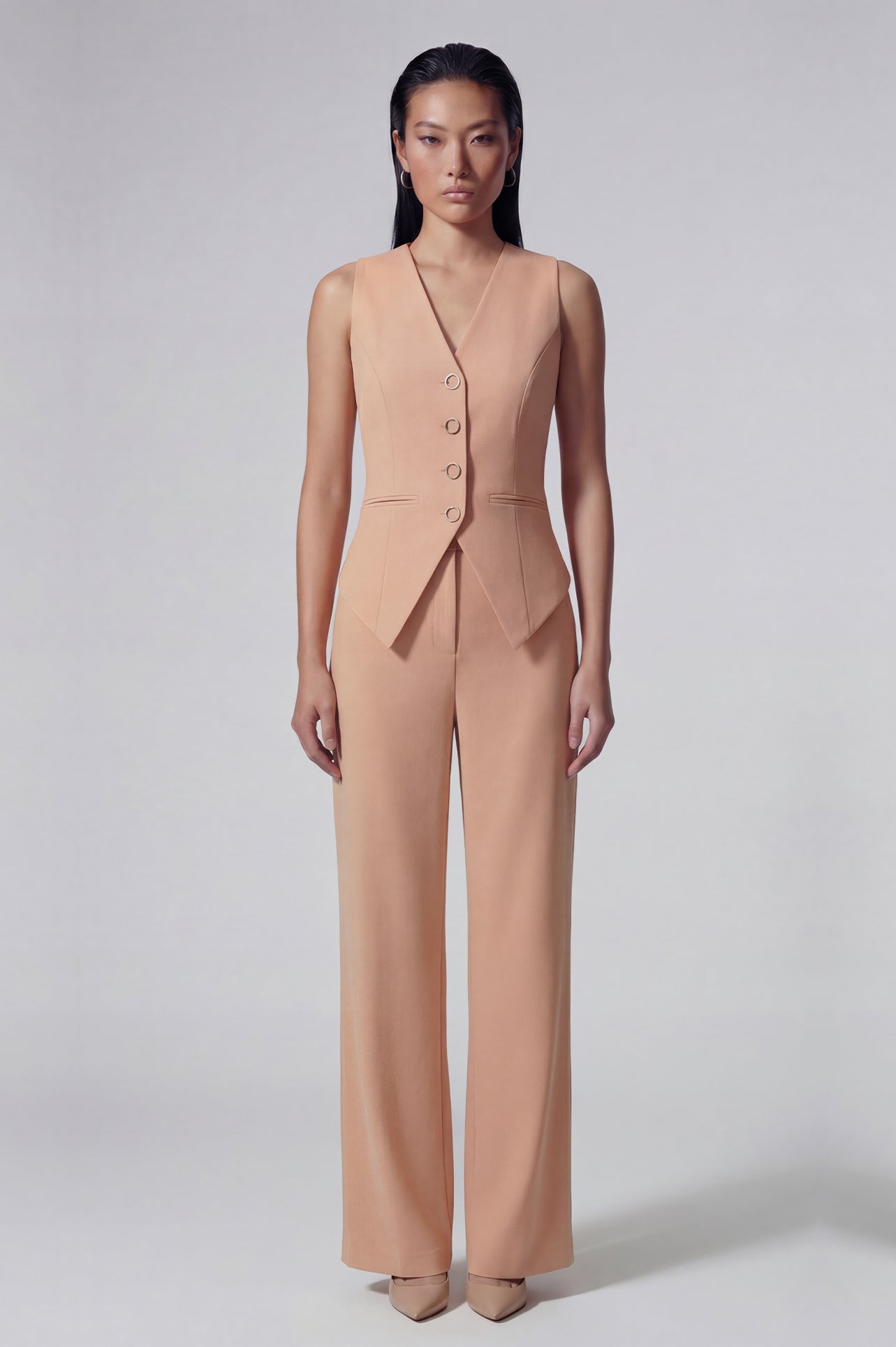 A professional woman wearing sophisticated apricot-colored high-waisted straight-leg trousers, featuring a unique pointed waistband design for a tailored executive office look.