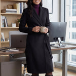 A professional woman wearing a sophisticated black long-sleeve coat dress, featuring an elegant tie-waist belt and notched lapels, styled over a white shirt for a polished executive business look.