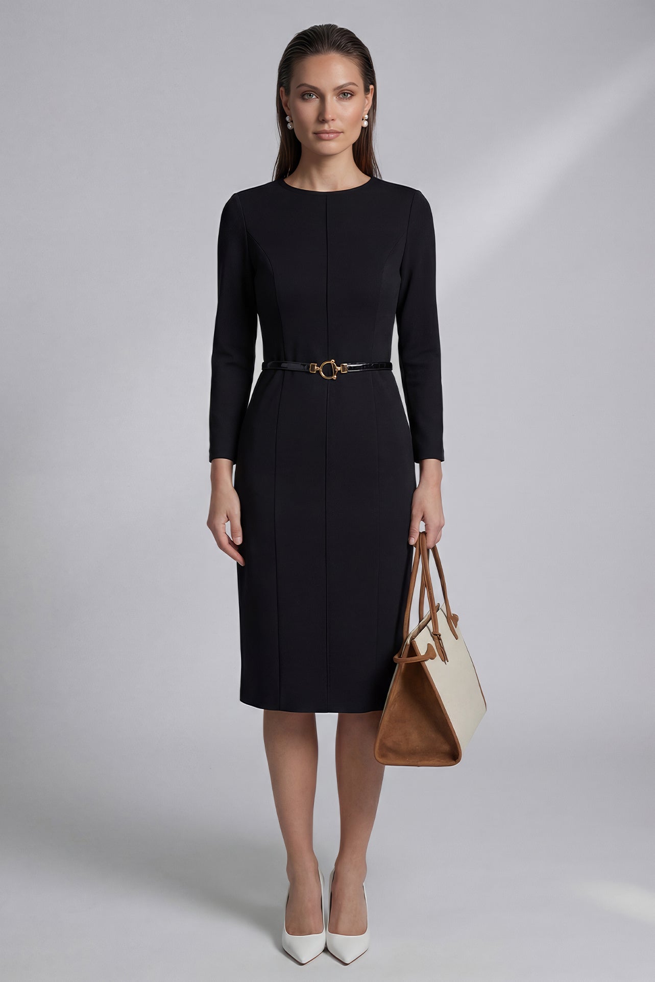 A professional woman wearing a sophisticated black long-sleeve sheath dress, featuring a classic crew neckline and a slim black belt with a gold buckle for a polished executive office look.