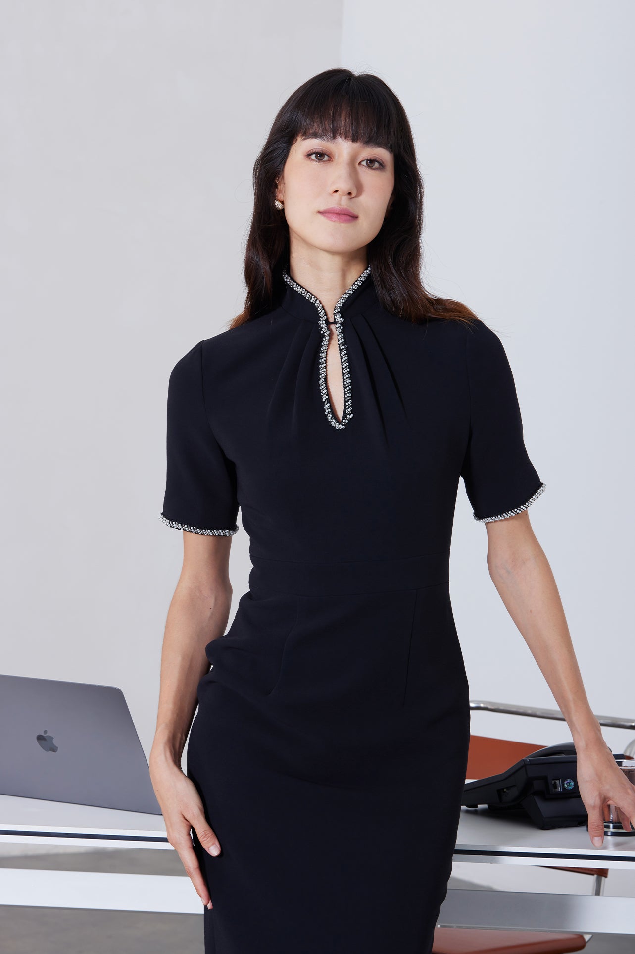 An elegant woman wearing a sophisticated black short-sleeve sheath dress, featuring a traditional mandarin collar with a modern keyhole neckline and delicate beaded trim details for a polished formal look.
