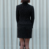 A detailed shot of a woman modeling a sophisticated black woven tweed mini skirt adorned with subtle shimmering crystals, tailored in a sleek high-waisted pencil cut.