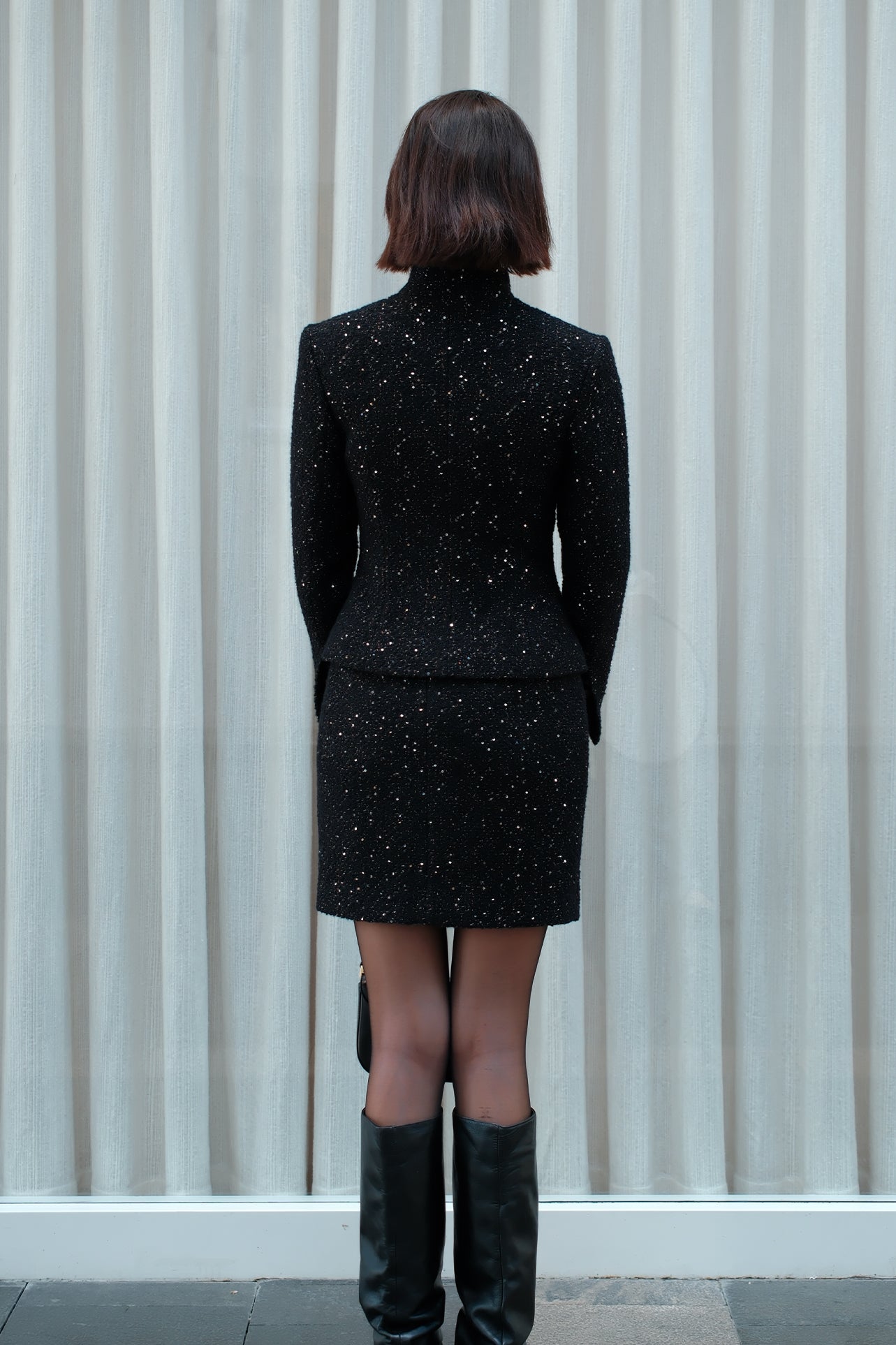 A detailed shot of a woman modeling a sophisticated black woven tweed mini skirt adorned with subtle shimmering crystals, tailored in a sleek high-waisted pencil cut.