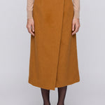 An elegant Asian woman posing in a luxurious camel wool two-piece suit featuring a sleeveless double-breasted longline vest cinched with a wide black belt, paired with a matching midi column skirt and black opera gloves.