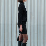 A chic woman wearing a luxurious black sparkle tweed tailored jacket featuring an authentic stand cheongsam collar, elegant horizontal pearl bar closures, and a flattering hourglass waistline.