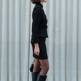 A chic woman wearing a luxurious black sparkle tweed tailored jacket featuring an authentic stand cheongsam collar, elegant horizontal pearl bar closures, and a flattering hourglass waistline.