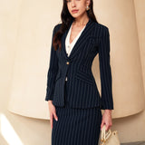 A professional woman wearing a sophisticated navy blue pinstripe suit, featuring a tailored single-button blazer and a matching midi pencil skirt with a front slit for an elegant executive office look.