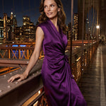 A professional woman modeling an elegant deep purple satin wrap midi dress, featuring a sophisticated surplice V-neck, cap sleeves, and a chic side bow tie for a quiet luxury evening or office look.