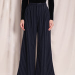 A professional woman wearing sophisticated navy blue pinstripe wide-leg trousers, featuring a high-waisted tailored fit and elegant vertical stripes for a polished executive office look.