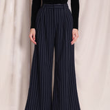 A professional woman wearing sophisticated navy blue pinstripe wide-leg trousers, featuring a high-waisted tailored fit and elegant vertical stripes for a polished executive office look.