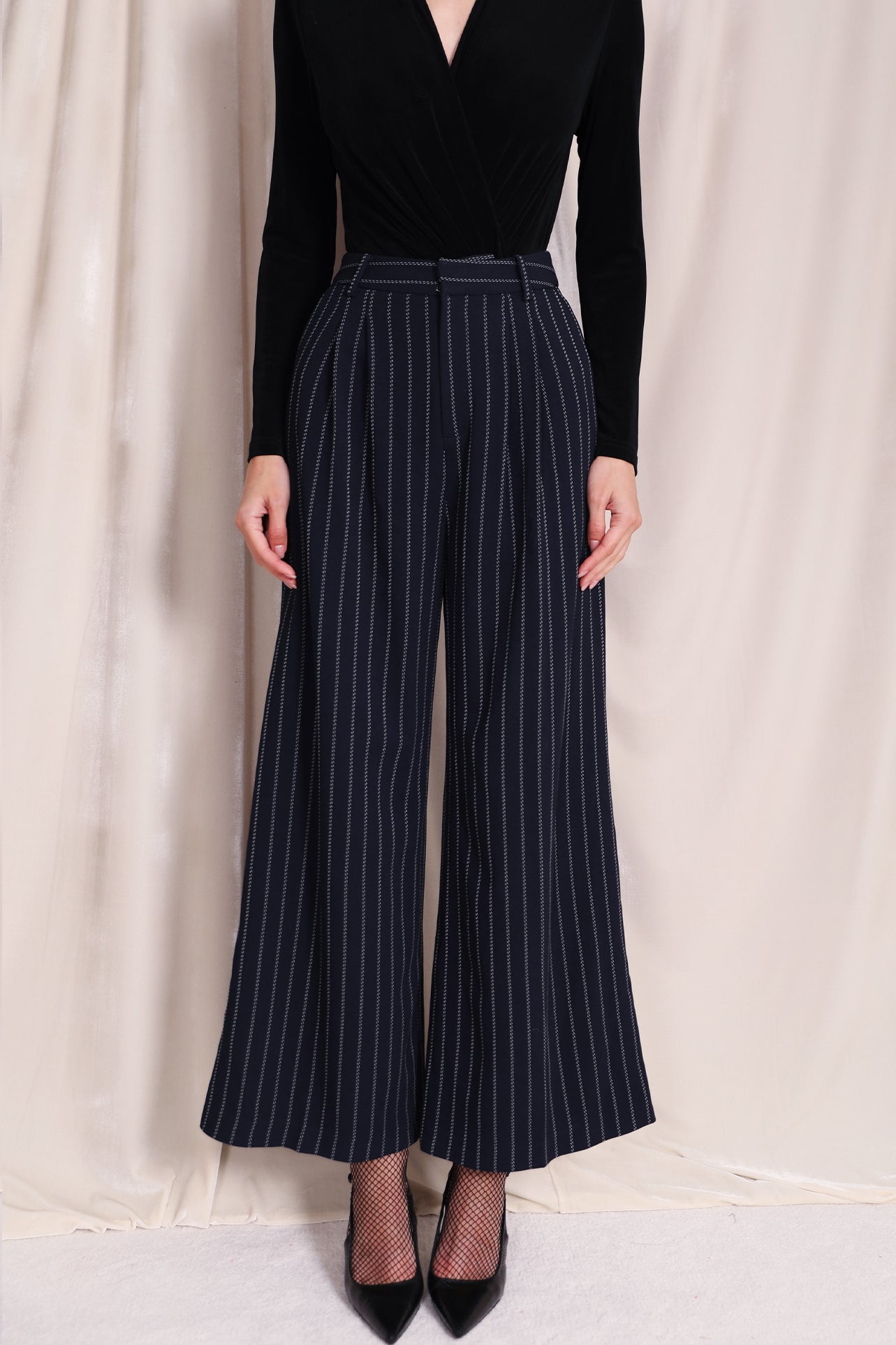 A professional woman wearing sophisticated navy blue pinstripe wide-leg trousers, featuring a high-waisted tailored fit and elegant vertical stripes for a polished executive office look.
