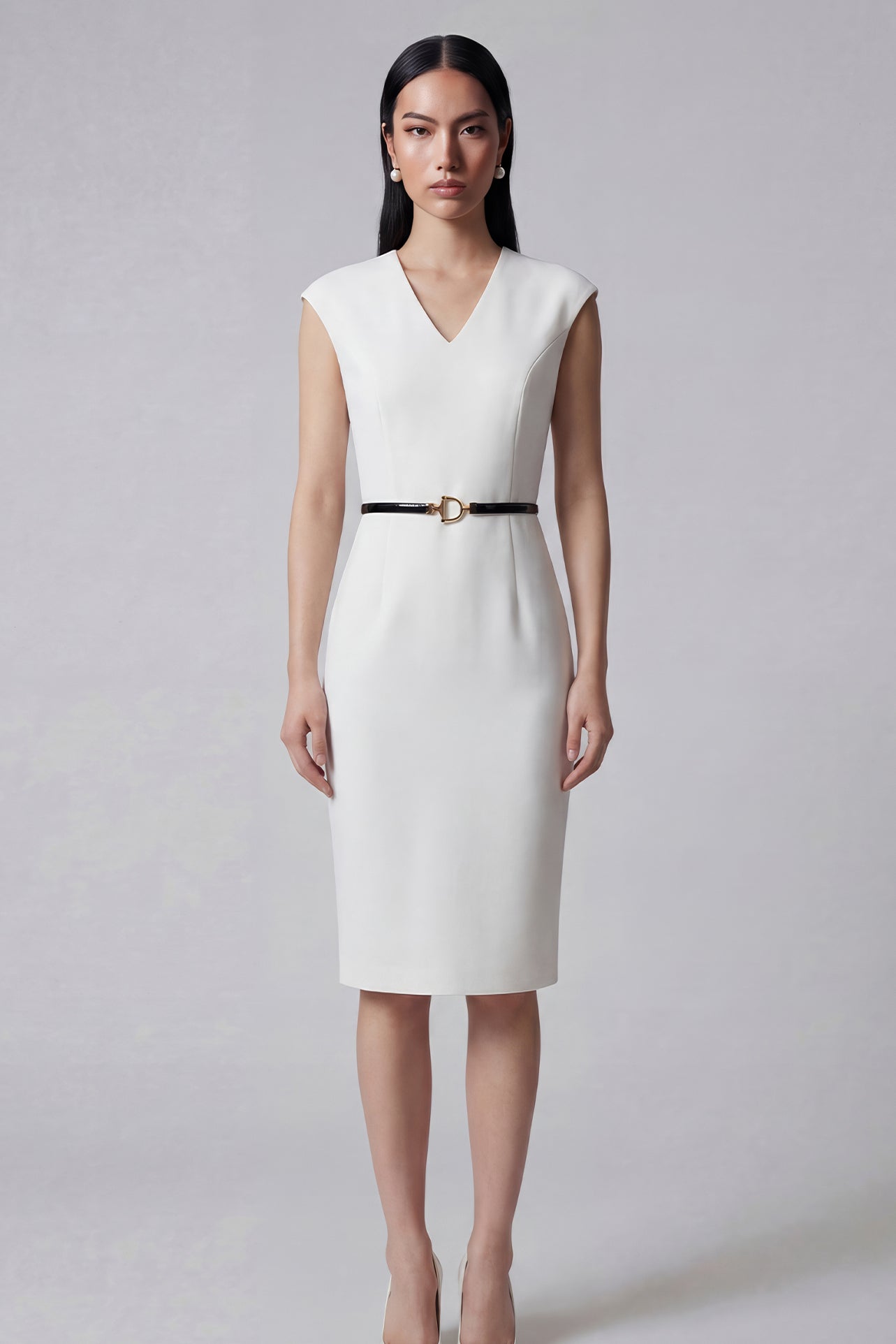 A professional woman wearing a sophisticated solid white sleeveless sheath dress, featuring a flattering V-neckline and an elegant thin black belt with a gold buckle for a polished executive office look.