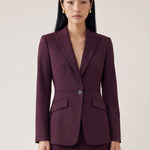  A professional woman wearing glasses and an elegant deep burgundy skirt suit featuring a sculptural stand-up lapel blazer with a single-button closure, tailored flap pockets, and a matching high-waisted pencil skirt.