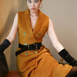 A chic professional woman wearing a tailored camel double-breasted longline suit vest featuring classic notch lapels and flap pockets, layered over a soft beige turtleneck sweater for a sophisticated quiet luxury look.