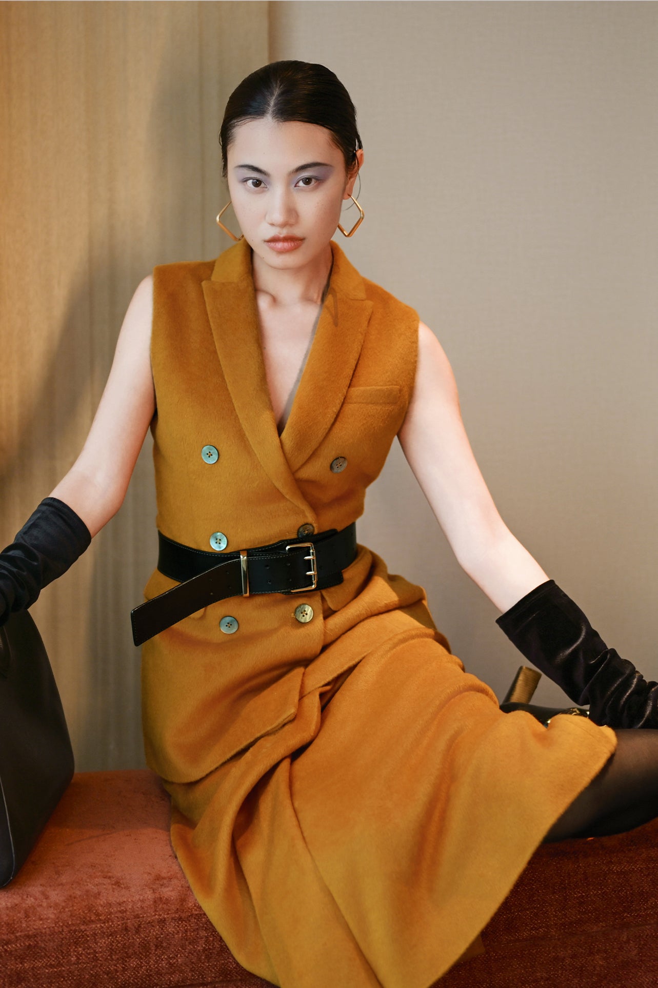 A chic professional woman wearing a tailored camel double-breasted longline suit vest featuring classic notch lapels and flap pockets, layered over a soft beige turtleneck sweater for a sophisticated quiet luxury look.
