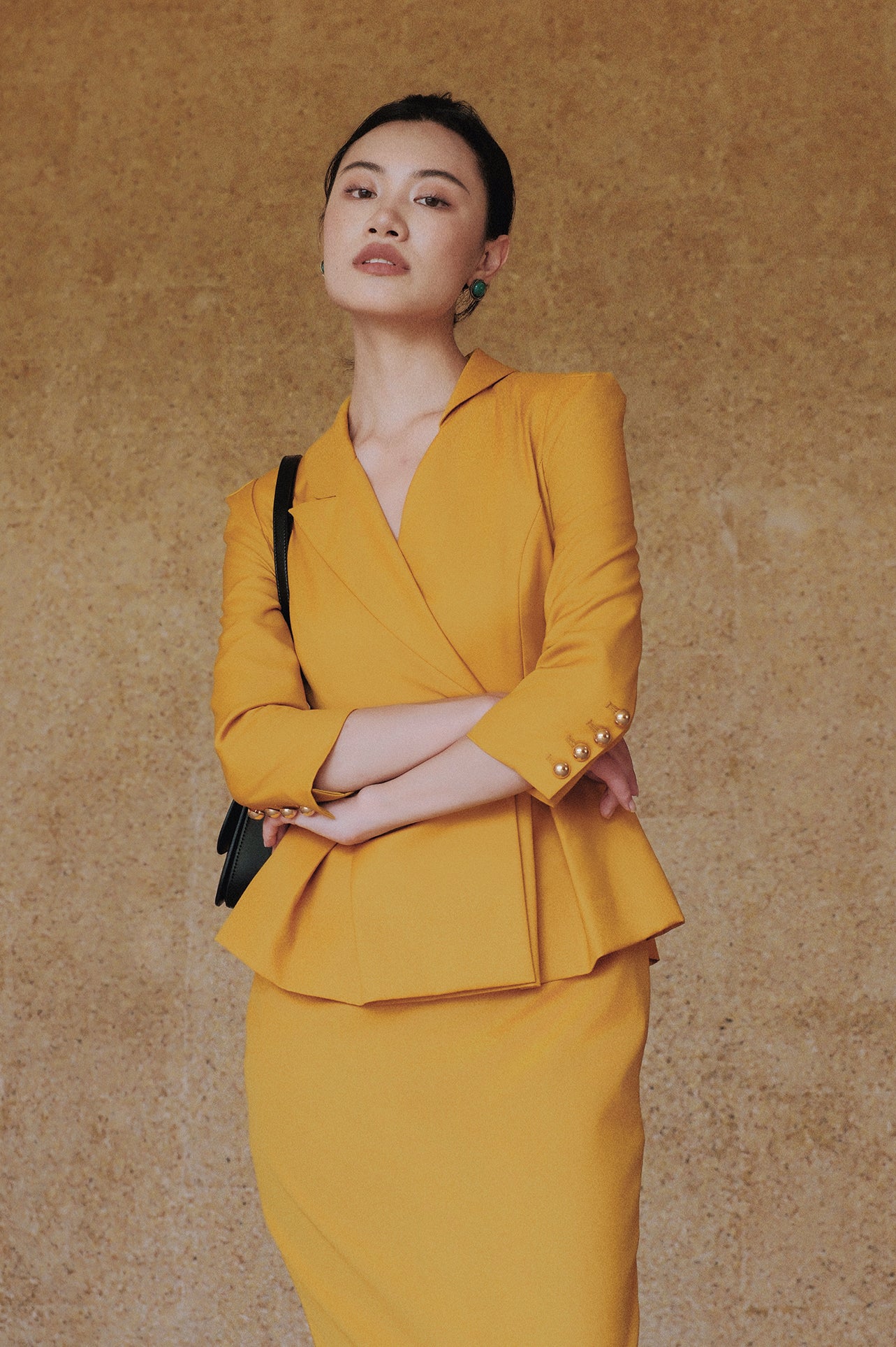 A style comparison of two elegant women's skirt suit sets featuring three-quarter sleeve blazers with single-button closure and pleated peplum hems, paired with matching pencil skirts in mustard yellow and deep teal blue.