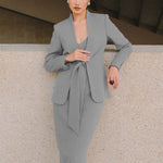 A beautiful professional model wearing an elegant grey pinstripe collarless blazer featuring a distinctive tie-front knot at the waist, styled with a crisp white collared shirt underneath for a modern corporate chic look.