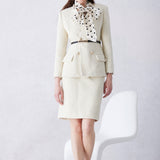 A professional woman wearing a sophisticated cream white tweed skirt suit, featuring a double-breasted blazer with gold buttons, a slim black belt, and an elegant polka dot pussy bow tie for a polished French chic office look.