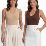 A professional woman modeling a sleeveless chocolate brown top and cream wide-leg pleated trousers, styled with a patterned yellow silk scarf and bold gold jewelry for a sophisticated office aesthetic.