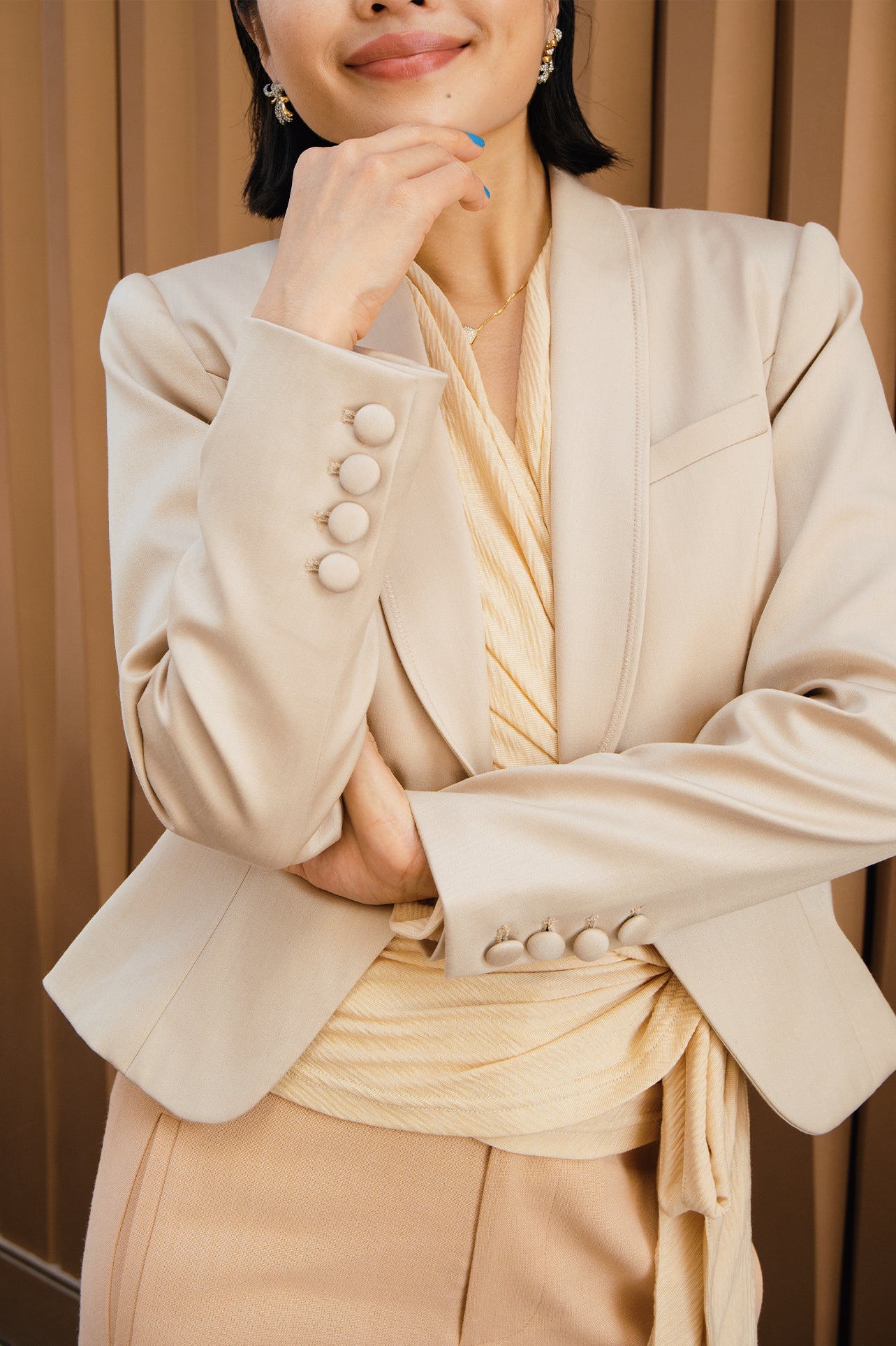 A professional woman modeling a luxurious champagne satin blazer featuring a soft shawl lapel and a single-button closure, elegantly paired with high-waisted white trousers for a sophisticated quiet luxury look.