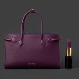 A sophisticated plum purple tote bag crafted from premium pebbled leather, displayed next to a matching shade of luxury lipstick, representing an elegant executive fashion set.