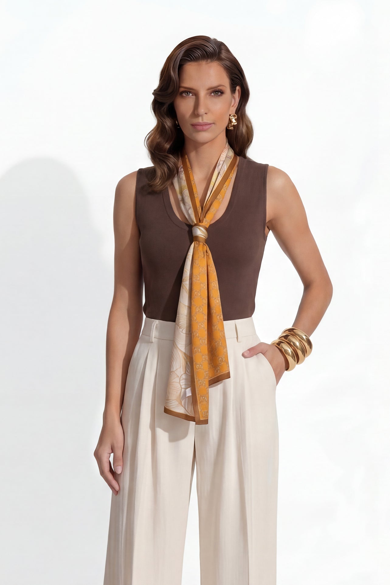 A professional woman modeling a sleeveless chocolate brown top and cream wide-leg pleated trousers, styled with a patterned yellow silk scarf and bold gold jewelry for a sophisticated office aesthetic.