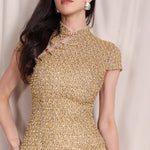 A professional woman wearing a stunning luxurious gold sequined modern qipao dress, featuring a traditional mandarin collar, short cap sleeves, and a slim-fit floor-length silhouette for a formal evening gala.