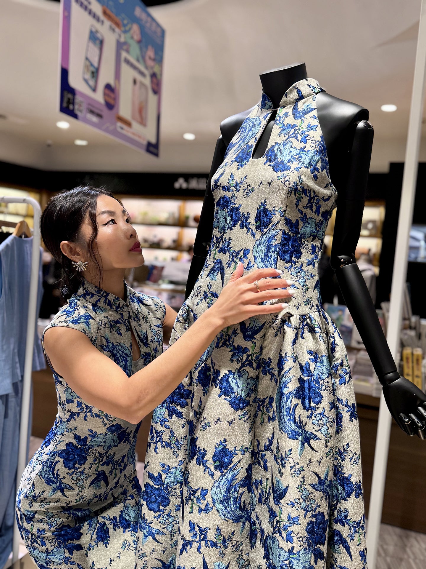 A professional woman wearing a sophisticated modern qipao dress, featuring a blue and white porcelain floral print, a mandarin collar with keyhole detail, and a slimming tailored fit for an elegant executive look.