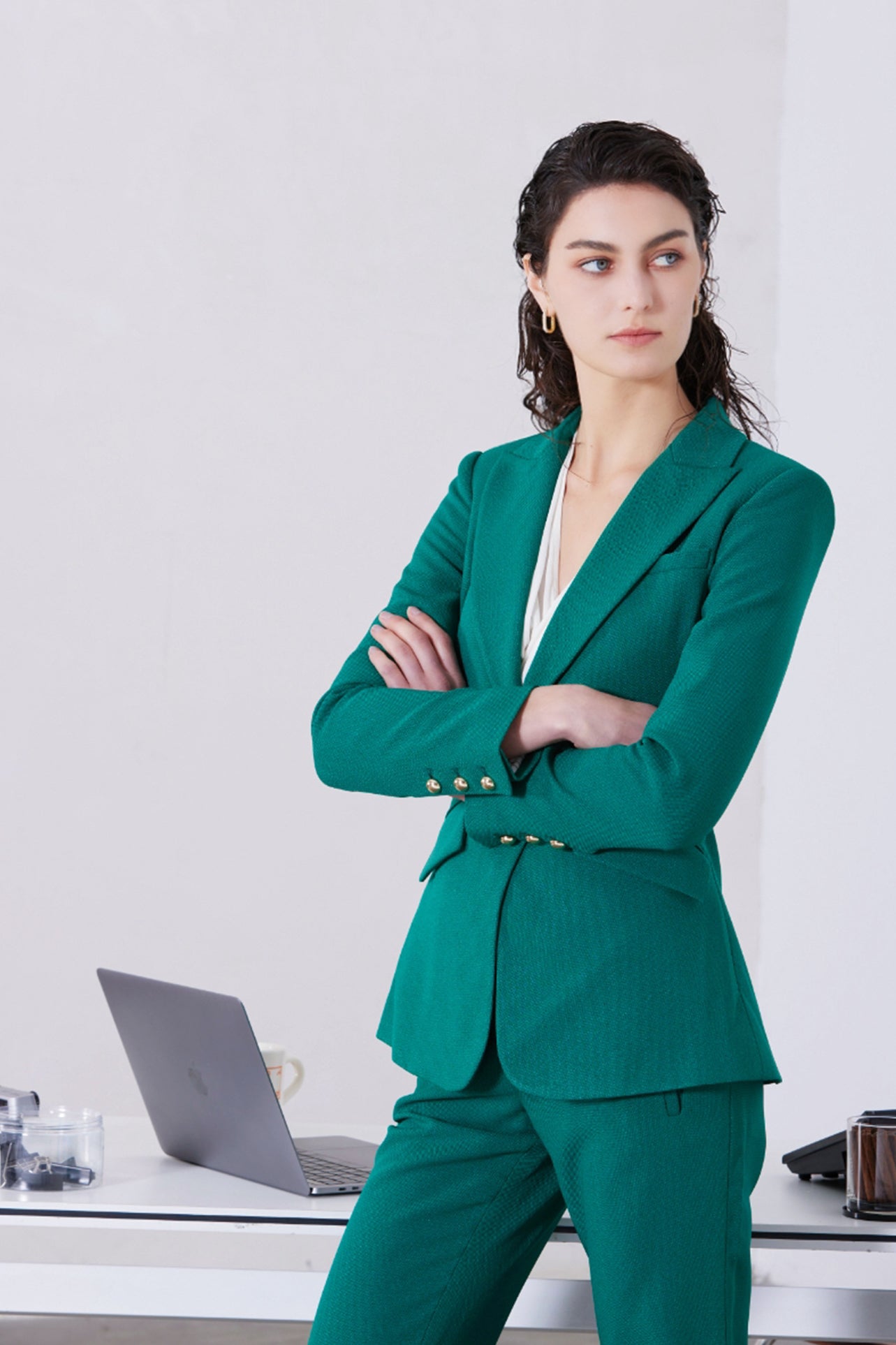 A professional woman wearing a sophisticated emerald green tailored blazer, featuring a slim-fit silhouette, notched lapels, and flap pockets, styled elegantly with a patterned silk scarf for a corporate office look.