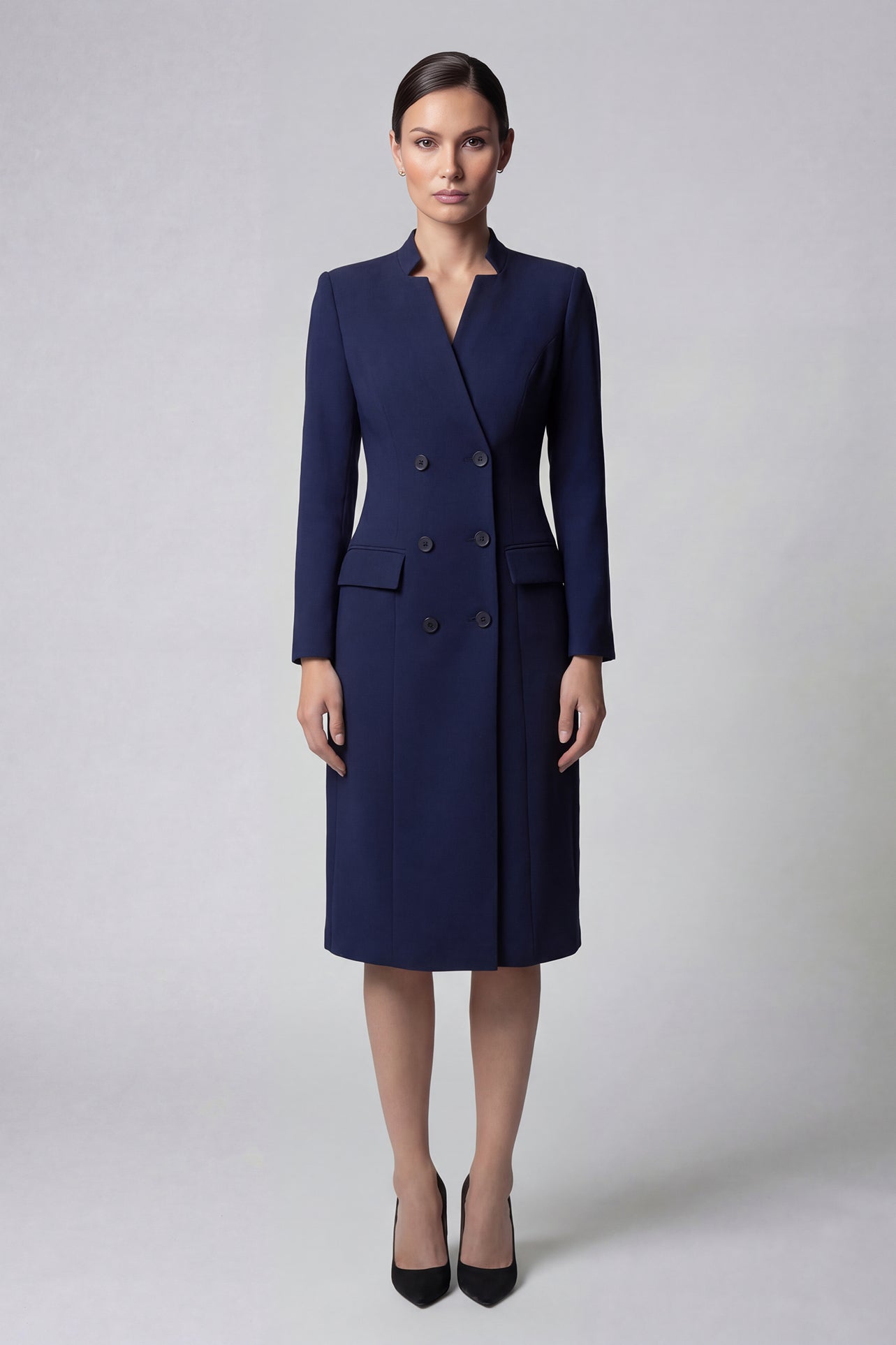 An elegant professional woman wearing a sophisticated navy blue double-breasted long coat dress, featuring a black waist belt and structured shoulders for a powerful executive look.