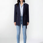 A professional woman wearing a sophisticated navy blue pinstripe blazer jacket, featuring a longline silhouette with a matching tie-waist belt and gold earring accents for an elegant executive office look.