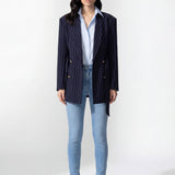 A professional woman wearing a sophisticated navy blue pinstripe blazer jacket, featuring a longline silhouette with a matching tie-waist belt and gold earring accents for an elegant executive office look.