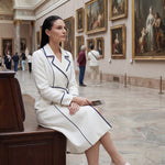 An elegant professional woman wearing a sophisticated white double-breasted coat dress featuring sharp navy blue contrast piping and a matching waist belt for a tailored executive look