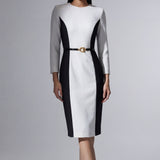 A professional woman wearing a sophisticated black and white color-block midi dress, featuring slimming side panels, long sleeves, and an elegant black belt with a gold buckle for a modern executive office look.