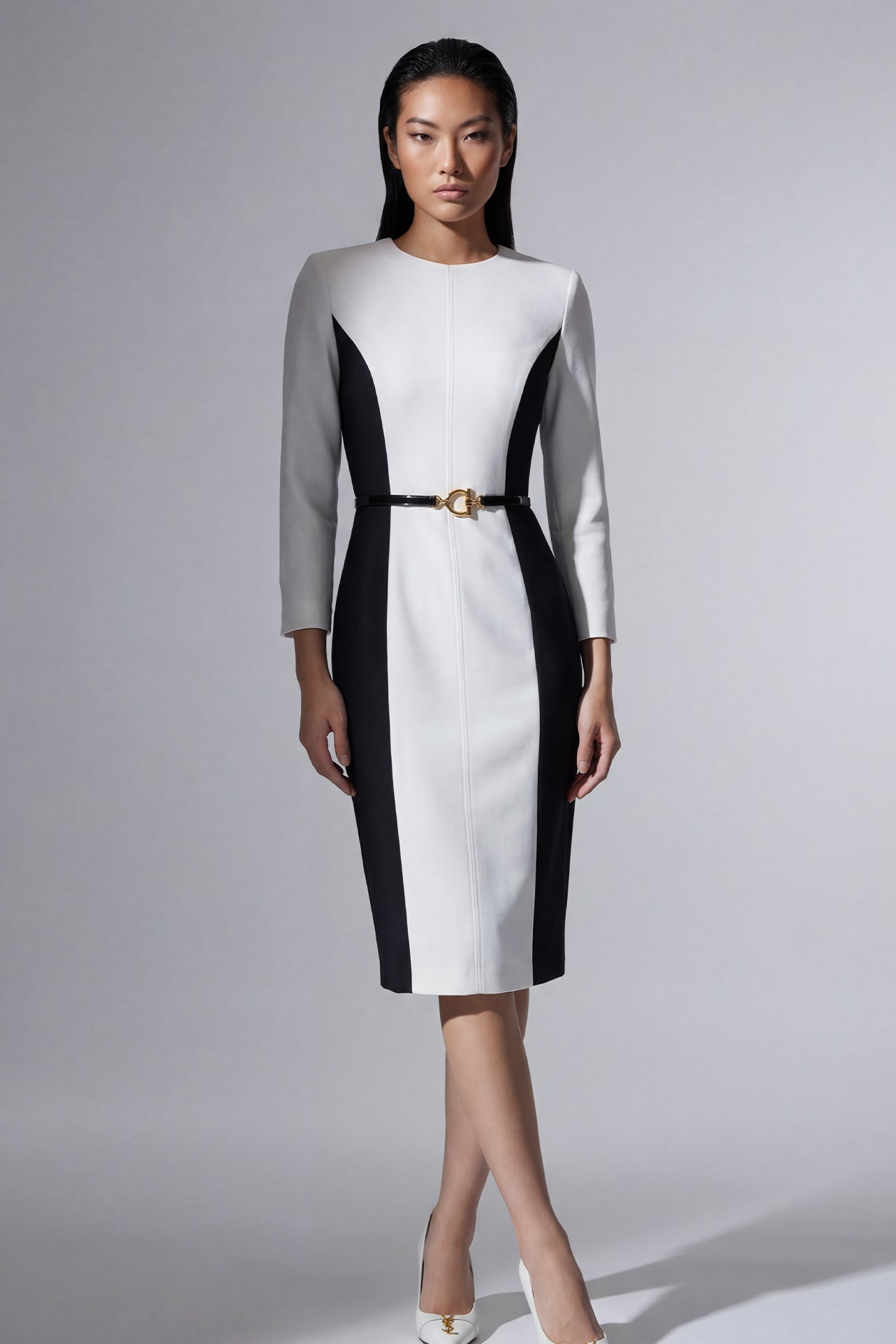 A professional woman wearing a sophisticated black and white color-block midi dress, featuring slimming side panels, long sleeves, and an elegant black belt with a gold buckle for a modern executive office look.