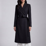 A professional woman wearing a sophisticated black long-sleeve coat dress, featuring an elegant tie-waist belt and notched lapels, styled over a white shirt for a polished executive business look.