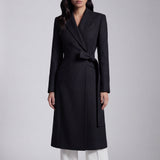 A professional woman wearing a sophisticated black long-sleeve coat dress, featuring an elegant tie-waist belt and notched lapels, styled over a white shirt for a polished executive business look.