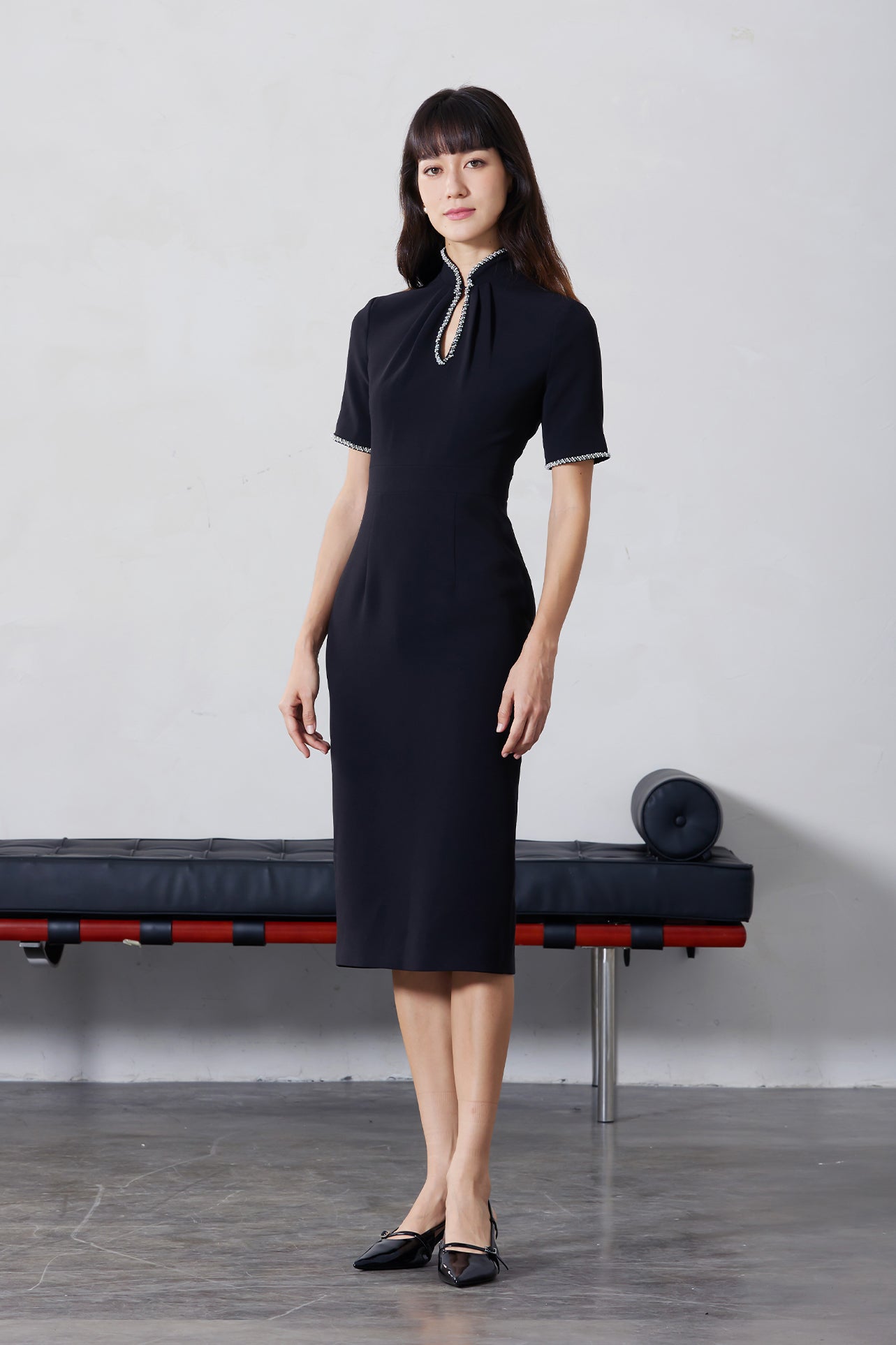 An elegant woman wearing a sophisticated black short-sleeve sheath dress, featuring a traditional mandarin collar with a modern keyhole neckline and delicate beaded trim details for a polished formal look.