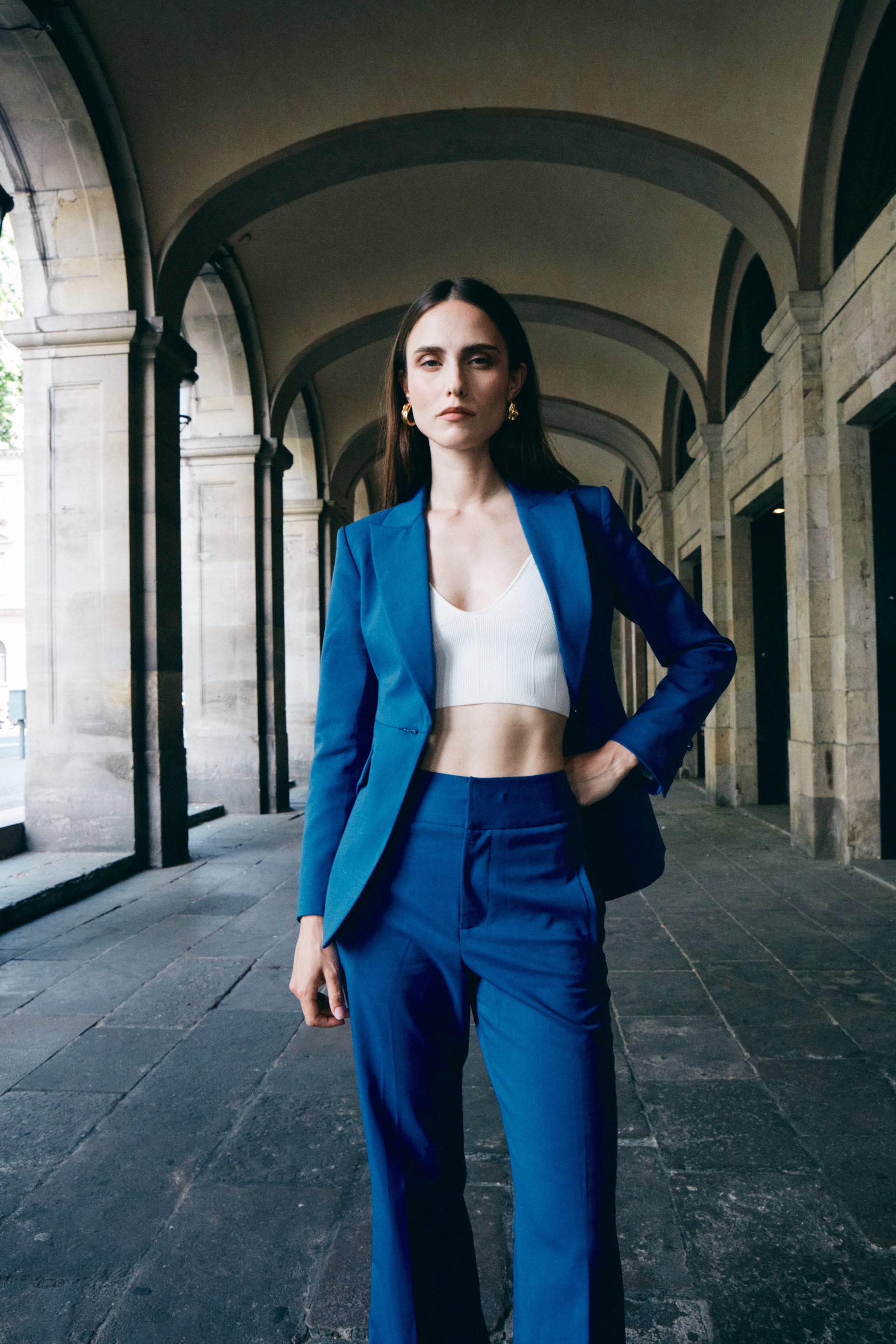 A professional woman wearing sophisticated royal blue high-waisted wide-leg trousers, featuring a tailored loose-fit silhouette for a modern and vibrant executive office look.