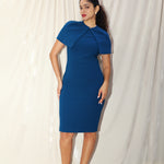 A professional woman wearing a sophisticated teal blue midi dress with an elegant cape-style overlay and structured shoulders, perfect for formal executive events and ceremonial occasions.