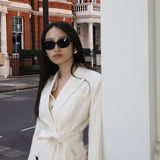 A professional woman wearing a sophisticated cream pinstripe blazer, featuring a double-breasted front with a chic waist-tie belt and notched lapels for a polished old money office look.