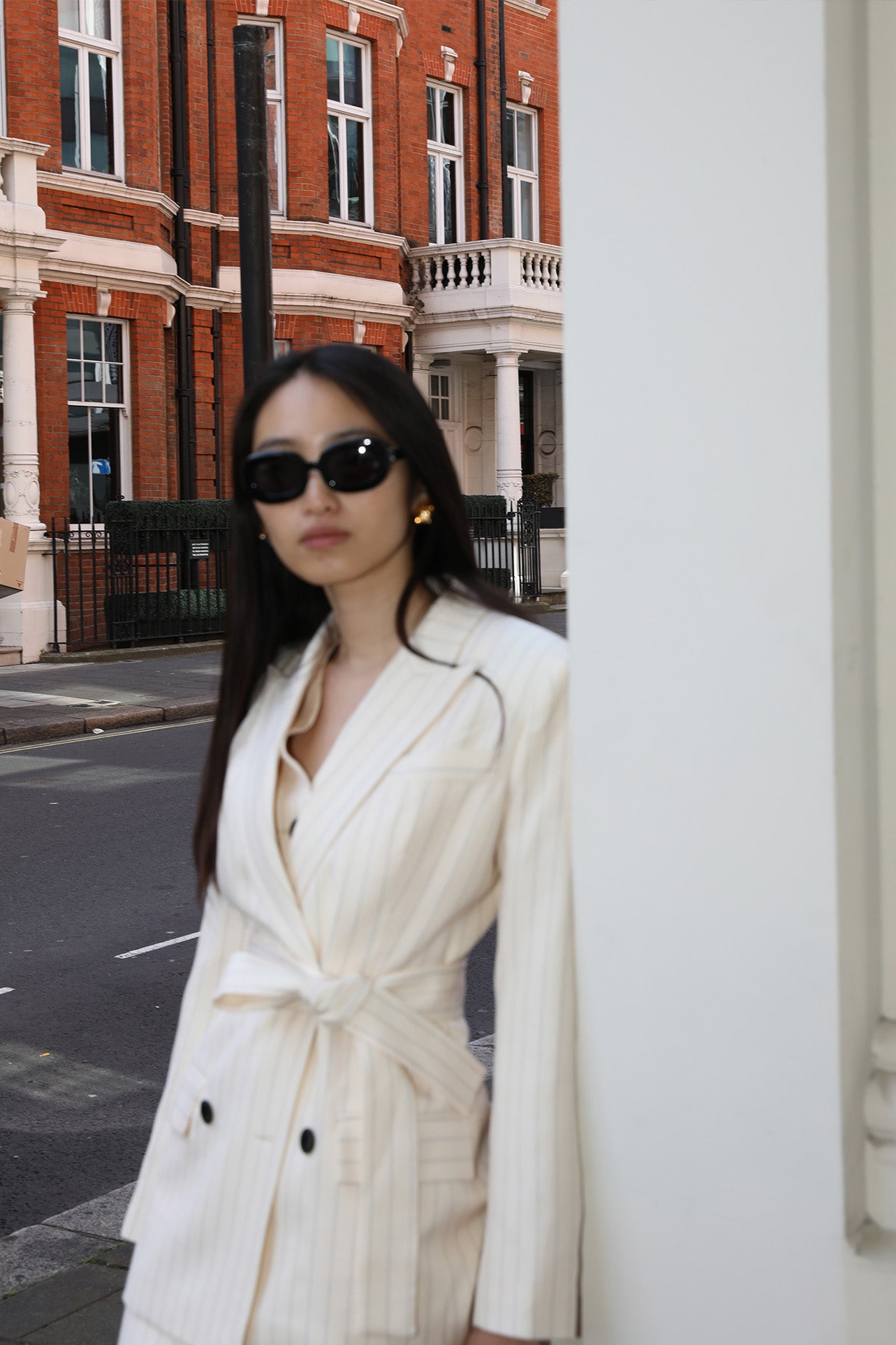 A professional woman wearing a sophisticated cream pinstripe blazer, featuring a double-breasted front with a chic waist-tie belt and notched lapels for a polished old money office look.