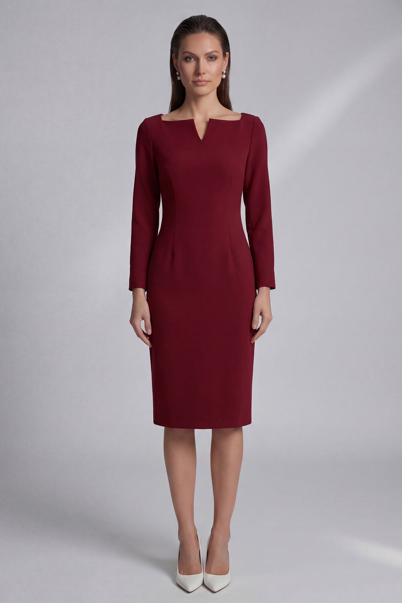 A professional woman wearing a sophisticated black long-sleeve midi dress, featuring a unique notched square neckline and a tailored slim-fit pencil silhouette for a polished executive office look.